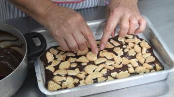 mulher colaca biscoitos sobre base de chocolate em forma. #paratodosverem