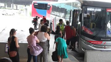 pessoas em fila para entrar em ônibus parado em baia de terminal rodoviário. #paratodosverem 