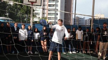 aluno joga beach tennis. ele segura raquete atrás de rede. #paratodosverem