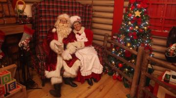 papai e mamãe noel sentados lado a lado em ambiente decorado para o natal. #paratodosverem 