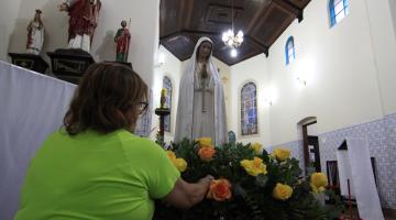 mulher arruma arranjo de flores na frente da santa #paratodosverem