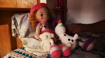 boneca e bichos de pelúcia sobre uma cama. #paratodosverem