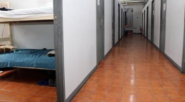 corredor com várias portas fechadas. Em primeiro plano, à esquerda, a porta de um quarto está aberta. Aparece uma cama beliche. #paratodosverem