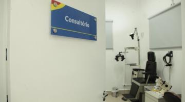 Porta do consultório entreaberta com cadeira oftalmológica ao fundo. #pracegover