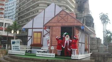 papai noel e mamães noel na frente da casinha na praça #paratodosverem