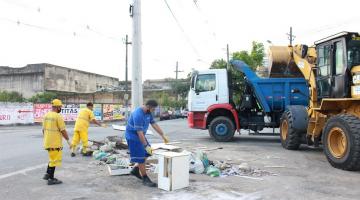 equipe de limpeza urbana está recolhendo entulho em calçada ao lado de trator e caminhão. #paratodosverem