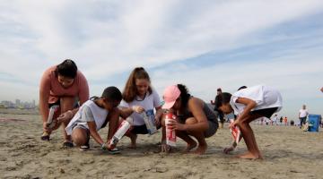 crianças recolhendo lixo na areia #paratodosverem