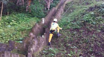 Homem escala morro realizando capinação. #paratodosverem