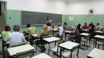 alunos adultos estão sentados em sala de aula. Professora está em pé falando ao grupo. #paratodosverem