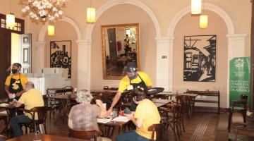 Garçom serve pessoas na mesa dentro de restaurante #paratodosverem