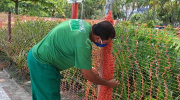 Funcionário instala cerca plástica diante do jardim da orla. #Paratodosverem