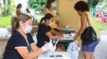 mulher se aproxima de mesas onde são feitos os cadastros para distribuição das cestas #paratodosverem 