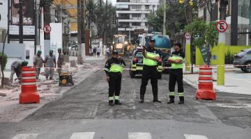 agentes de trânsito estão parados em rua em obras ao lado de cones. #paratodosverem