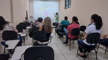 pessoas etão sentadas em cadeiras escolares, de costas para foto, assistindo palestra. #paratodosverem 