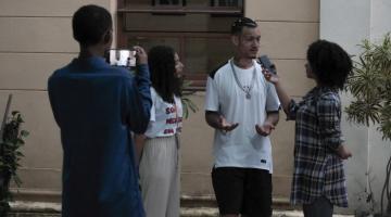 jovem está em pé sendo entrevistado por estudantes. #paratodosverem 