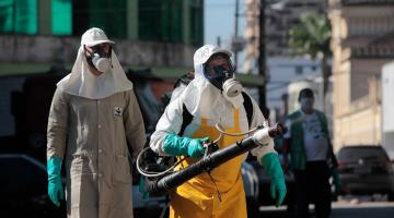 Dois homens com máscaras manuseiam equipamento em rua #paratodosverem