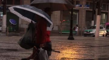Duas pessoas caminham com guarda chuva em rua à noite. #Paratodosverem