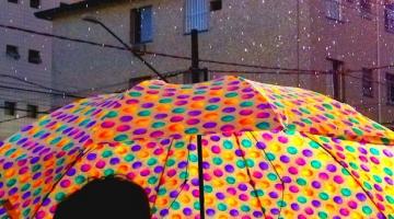 uma pessoa de costas para a foto está segurando um guarda chuva aberto na rua. #paratodosverem