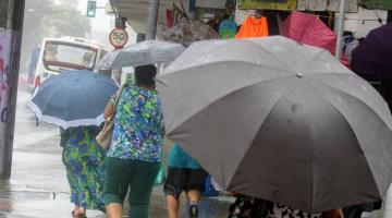 pessoas andando na rua em dia de chuva usando guarda-chuva. #paratodosverem