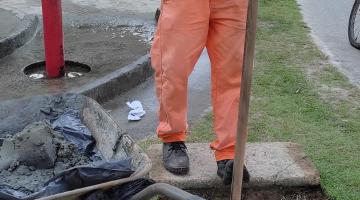homem limpa caixa de drenagem ao lado de chuveirinho. #paratodosverem