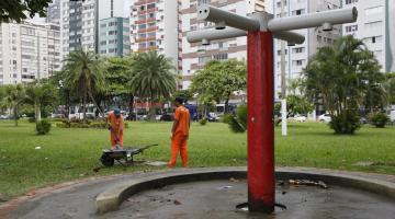 chuveirinho em primeiro plano e dois homens ao lado de carrinho de mão. Eles se movimentam para limpar caixa de deposição de areia. #paratodosverem