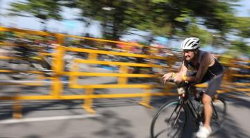 ciclista pedala em velocidade. Imagem ao fundo, na avenida, está desfocada, demonstrando a velocidade. #paratodosverem