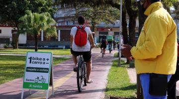 Agente de trânsito observa passagem de ciclista na ciclovia ao lado de placa com a inscrição Uma bike a mais Um carro a Menos. #pracegover