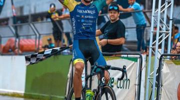Atleta, sobre a bicicleta, levanta os braços na chegada. #pratodosverem