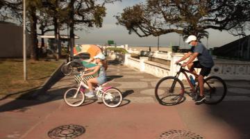 Pai e filha andando de bicicleta na ciclovia da praia. #paratodosverem