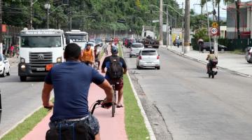 ciclistas pedalando em ciclovia. Carros estão rodando nas duas pistas entre a ciclovia. Uma pista vai, outra vem. #paratodosverem