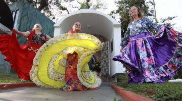 mulheres vestidas com roupas típicas ciganas, dançam em frente a uma gruta. O movimento da dança roda as sais dos vestidos que se abrem. #paratodosverem