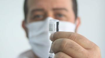 close de frasco de vacinação na mão de homem que usa máscara. #paratodosverem