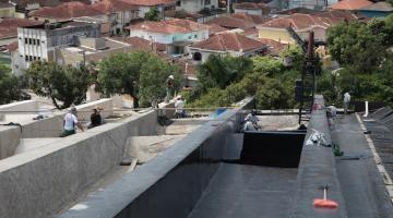 cobertura do teatro em obras, com homens trabalhando ao fundo e vista de prédios da cidade abaixo. #paratodosverem