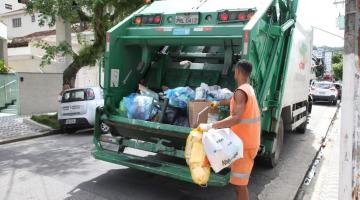 homem está colocando sacos de lixo dentro de caminhão compactador que está na rua. #paratodosverem