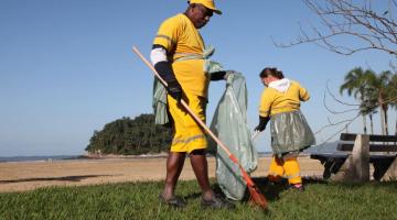 homem e mulher uniformizados removem folhas de jardim da orla. #paratodosverem