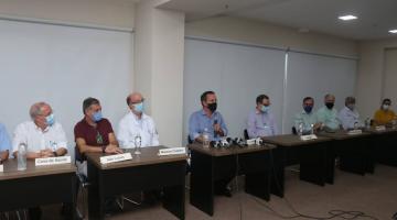 O secretário de saúde e diversos representantes do setor de saúde sentados em torno de mesas. 