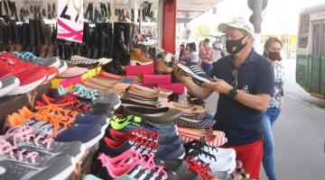 frente de loja com inúmeros pares de sapato em exposição. Um homem segura um pé de tênis. A rua está ao lado direito. #paratodosverem