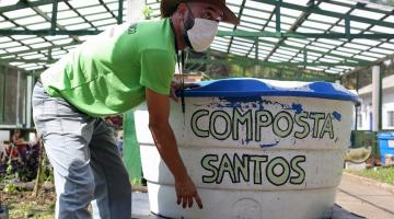 homem está com as  mãos em caixa de compostagem onde se lê Composta Santos. #paratodosverem