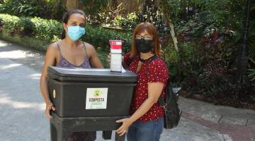 duas mulheres seguram composteiras juntas. Elas posam para a foto. #paratodosverem