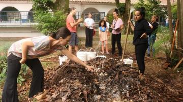 pessoas estão em um canteiro juntando material orgânico. #paratodosverem 