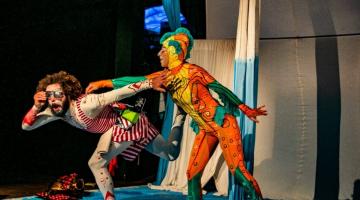 dois artistas com roupas coloridas no palco. #paratodosverem