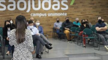 palestra sendo realizada em auditório, com pessoas sentadas e uma mulher de costas, em pé, falando ao público. #paratodosverem