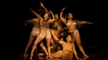 atrizes fazem acenos com as mãos pra cima em cena de teatro #paratodosverem 