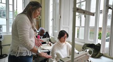 pessoas costurando com professora ao lado #paratodosverem