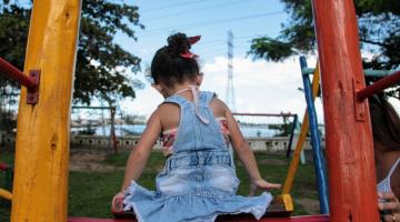 criança de costas para a foto sentada no topo de escorregador. #paratodosverem