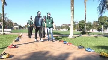 Agentes de força-tarefa estão em área aberta, um jardim. Nas laterias há chuteiras de futebol. #Paratodosverem