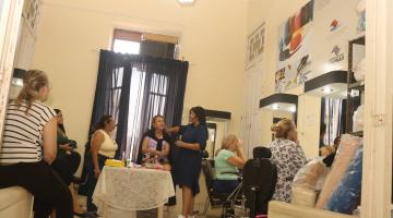 mulheres reunidas com mesa ao centro com produtos de maquiagem. #paratodosverem