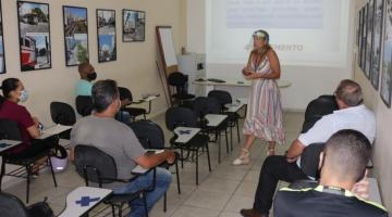 Professora, com máscara de proteção, dá aula para vários alunos sentados. #paratodosverem