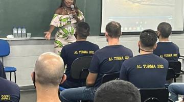 Mulher está em pé falando a um grupo de guardas que estão sentados em sala de aula. #paratodosveram