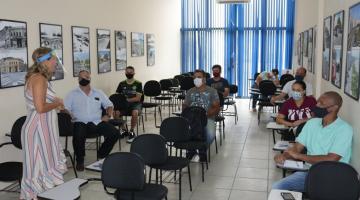 Sala de aula com professora em pé e alunos, adultos, sentados. #paratodosverem